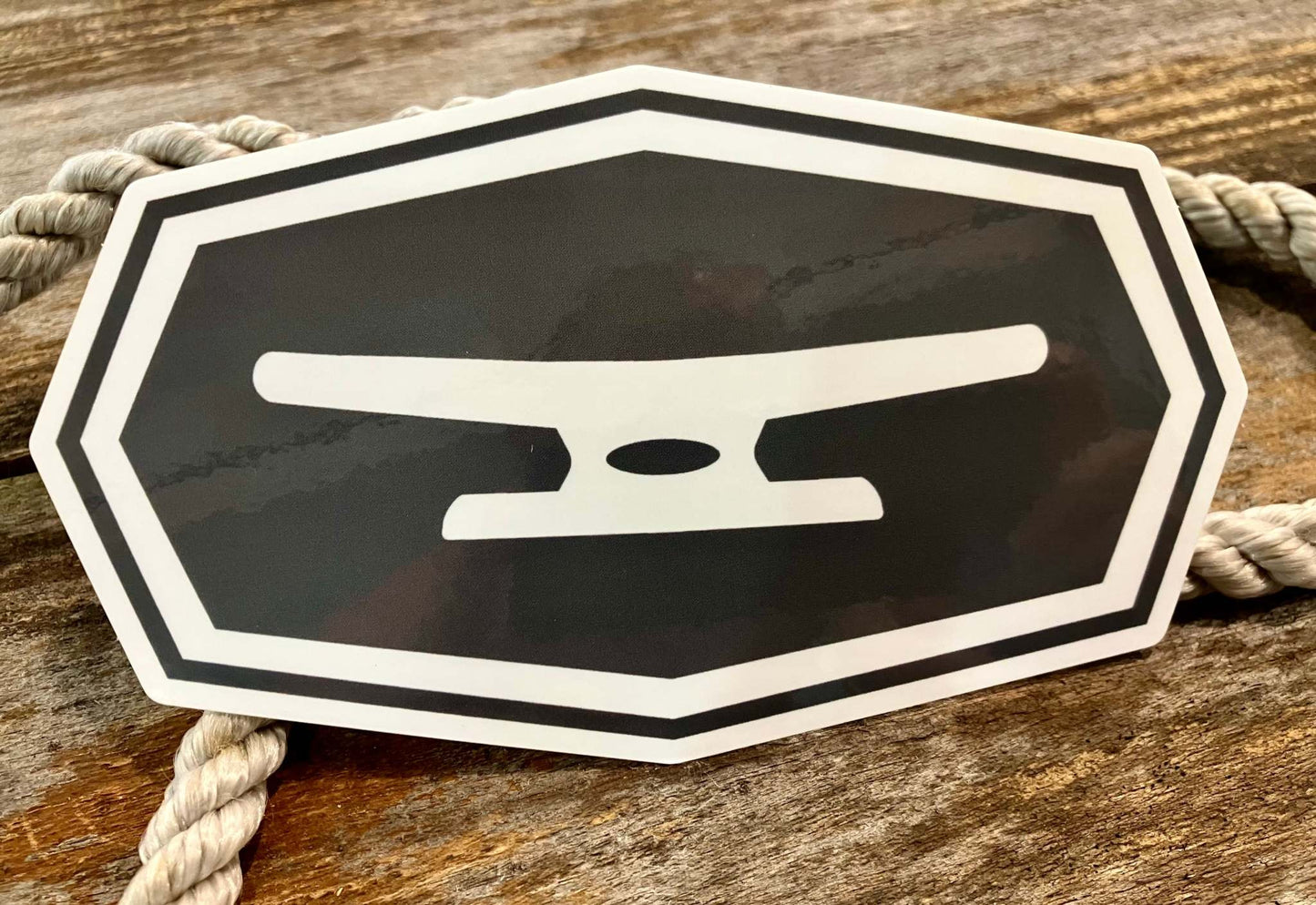 Klēt black and white anvil logo sticker on wooden background with rope detail