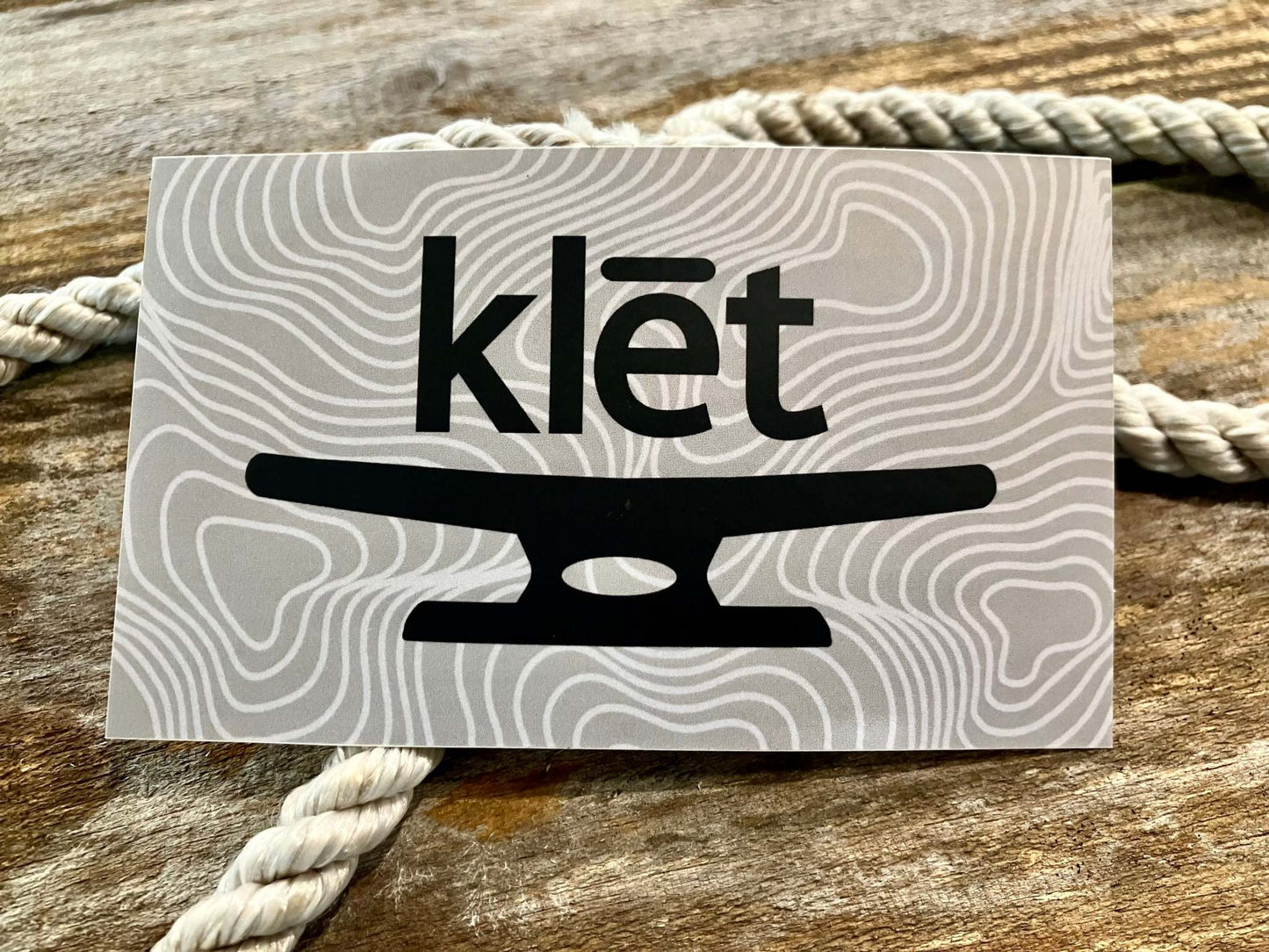 Klēt Open Sea 5-inch durable sticker with black maritime design on wavy gray background placed on rustic wood with rope details
