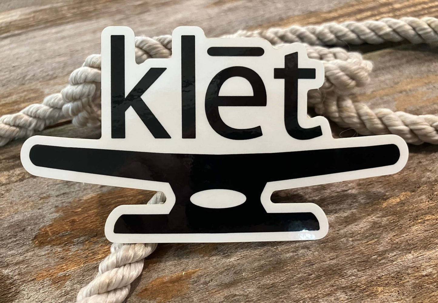 Klēt logo black and white sticker on wooden surface with rope background