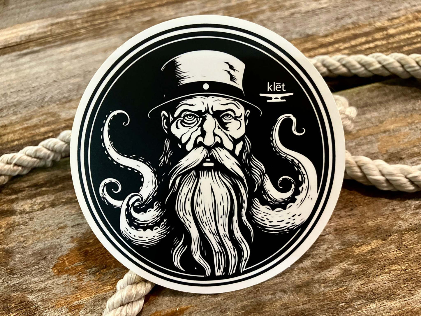 Black and white Klēt sticker featuring a bearded sailor with octopus tentacles on wooden background