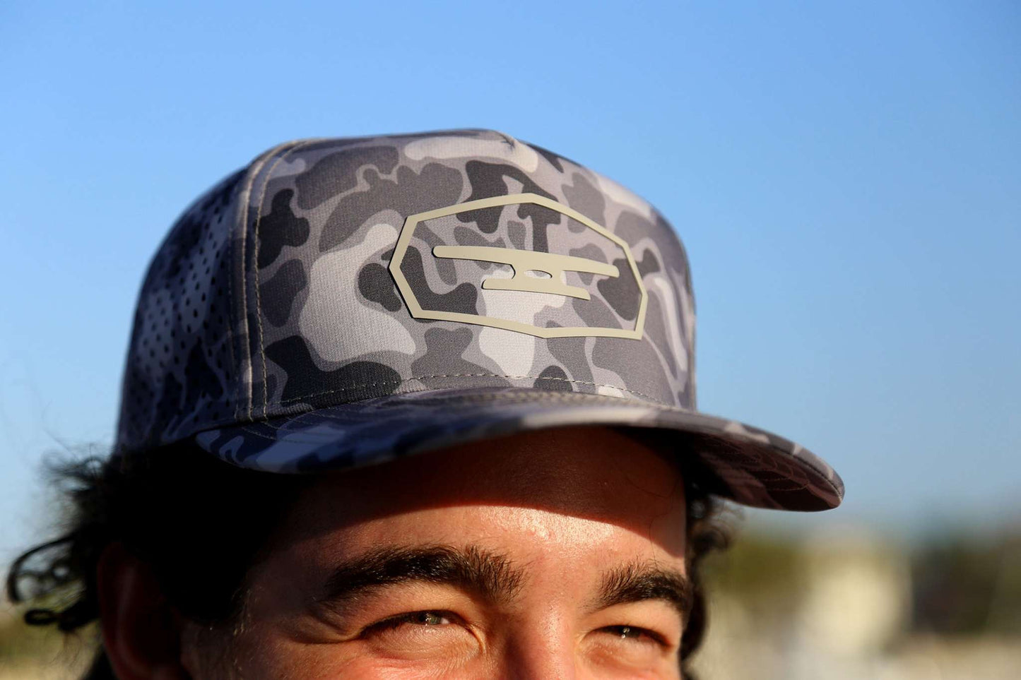 Man wearing Klēt Commodore Camo hat with gray and black camo pattern and logo patch against blue sky background Klēt - Commodore Camo