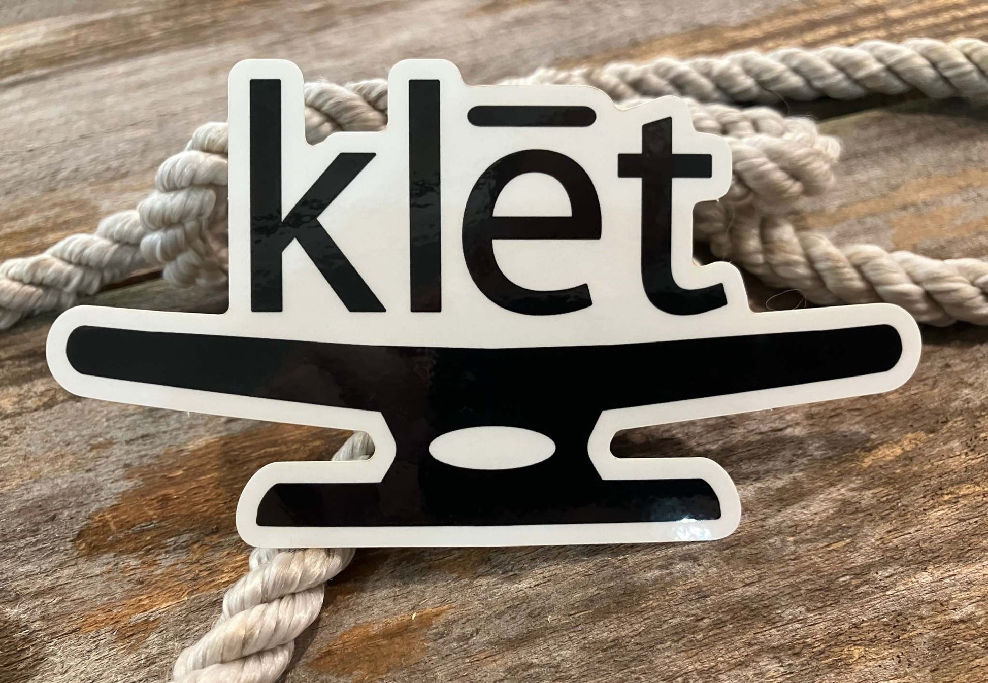 Klēt logo black and white sticker on wooden surface with rope background